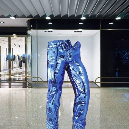 A reflective blue sculpture of jeans on display in a modern indoor gallery.