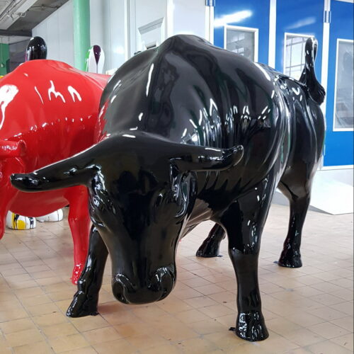 Two large bull sculptures, one painted black and the other red, displayed indoors with blue double doors in the background.