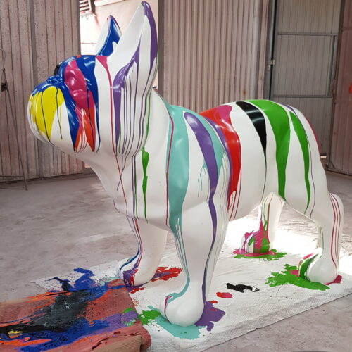 A large white bulldog statue covered in colorful paint drips standing indoors.