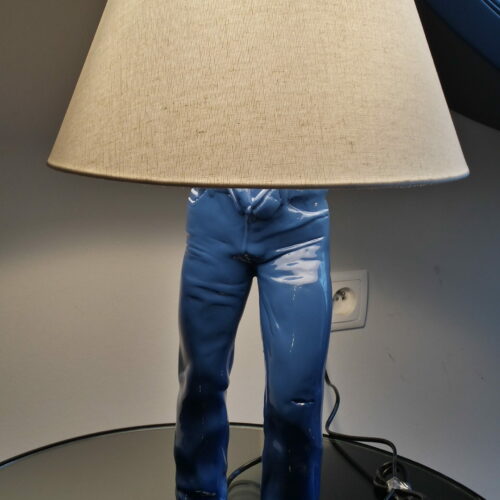 Table lamp in the shape of human legs wearing blue pants with a beige lampshade.