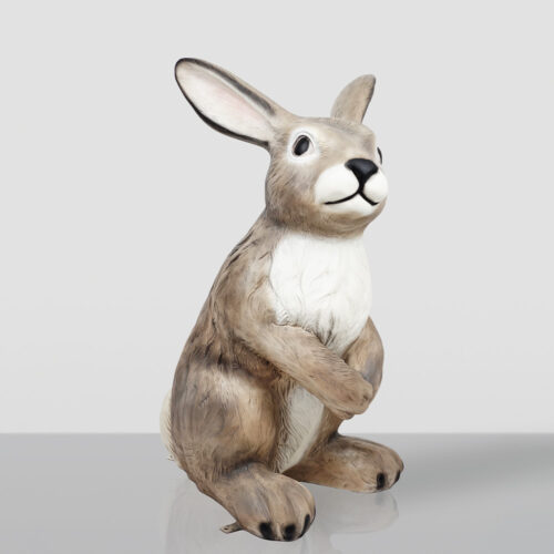 Realistic brown and white rabbit figurine sitting upright on a reflective surface against a plain light gray background.