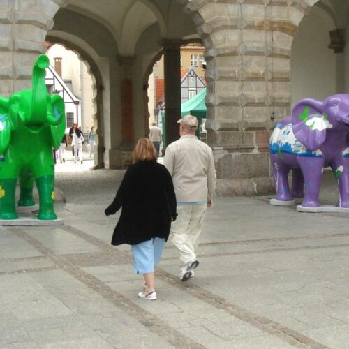 Two people walking under an archway with colorful elephant statues on each side.