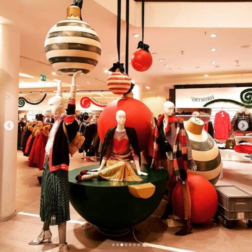 Christmas-themed store display with mannequins dressed in festive clothing and surrounded by oversized ornaments.