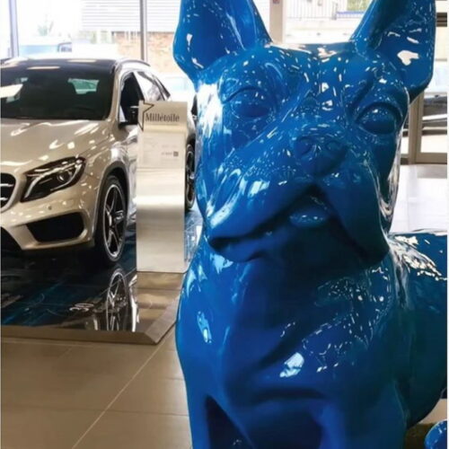 Large blue dog sculpture in a car showroom with a white luxury car in the background.
