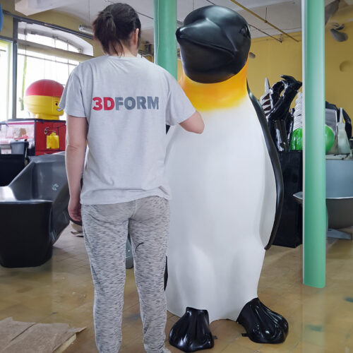 Person wearing a 3DFORM shirt working on a large penguin sculpture indoors.