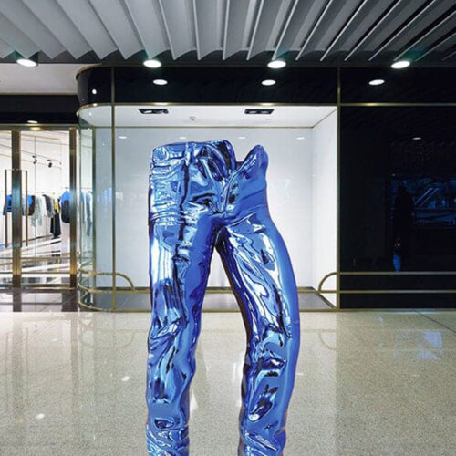 A sculpture of blue metallic pants displayed in a modern interior setting with glass doors and glossy floors.