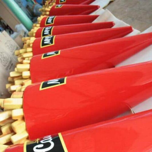 Row of bright red cricket bats with light wooden handles neatly lined up diagonally on a white surface