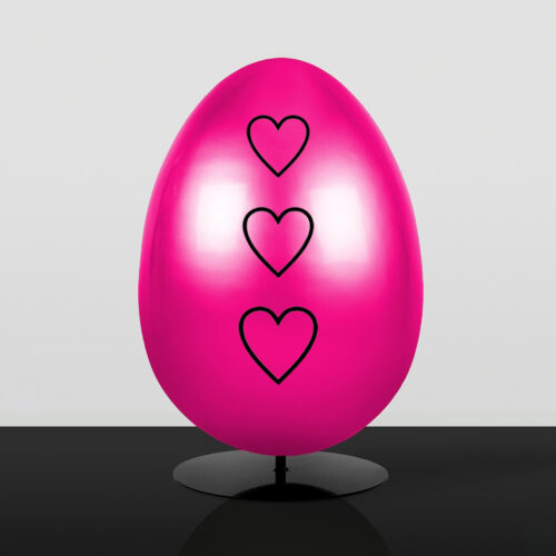Purple egg-shaped sculpture with a large golden heart on the front, displayed on a black circular stand against a light gray background.