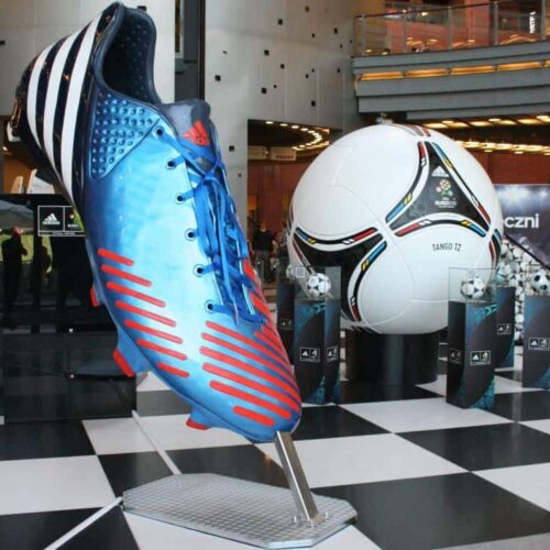Large blue and red Adidas soccer shoe model displayed next to an oversized Adidas Tango 12 soccer ball.
