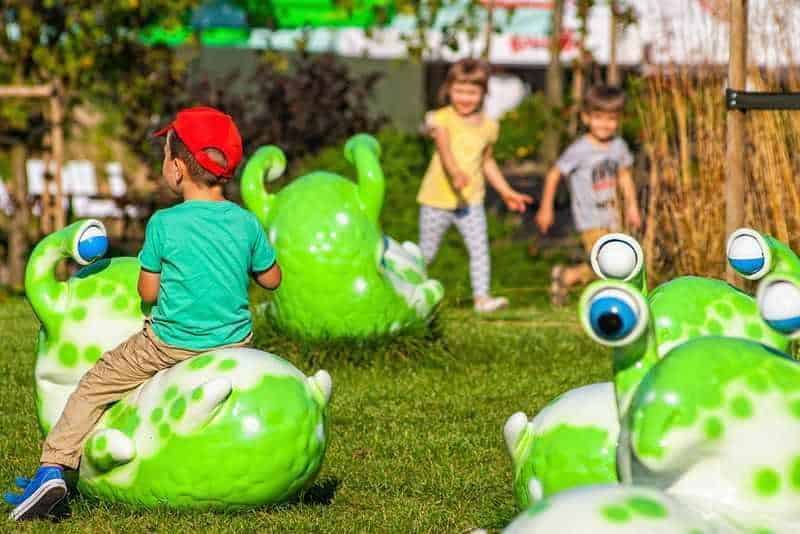 oryg_064490685_1129949550544944_1465385417682452480_o Children playing on large green snail sculptures in an outdoor playground.