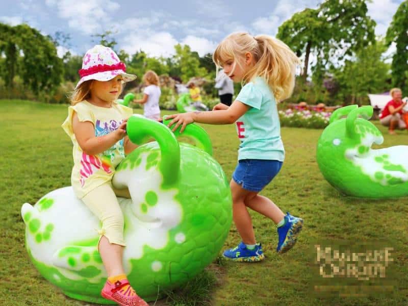 Figures in the amusement park 1 Dzieci bawiące się na zielonym trawniku z kolorowymi, zielono-białymi, dużymi zabawkami w kształcie ślimaków.