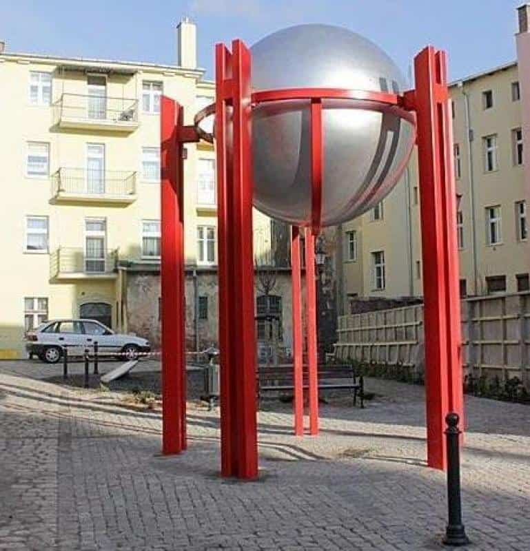 Large metallic sphere supported by bright red pillars in a courtyard.