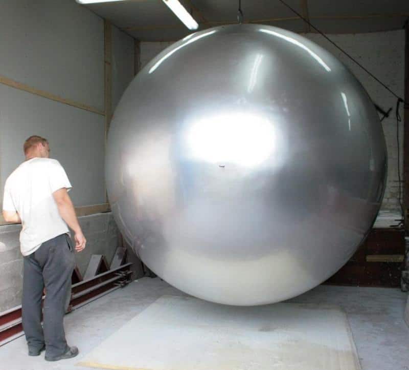 Mężczyzna stojący obok ogromnej, srebrnej kuli w hangarze.