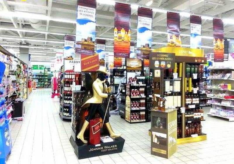 oryg_064490685_1129949550544944_1465385417682452480_o Supermarket aisle with extensive liquor displays, including prominent Johnnie Walker and Ricard stands, surrounded by shelves of alcoholic beverages.
