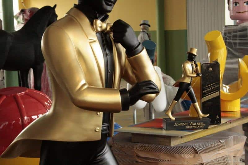 Large Johnnie Walker Figures 1 Złota figurka Johni Walker w złotym garniturze, obok mniejsza statuetka i pudełko.