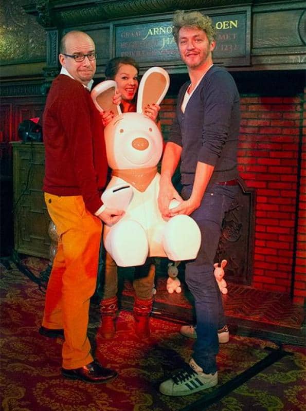 oryg_064490685_1129949550544944_1465385417682452480_o Three people posing with a large white bunny figurine in front of a fireplace.