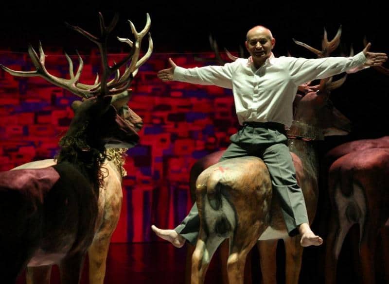 Stage design elements for the Dramatic Theatre of the Capital City of Warsaw 4 Mężczyzna siedzący na makiecie jelenia na scenie z czerwono-fioletowym tłem.