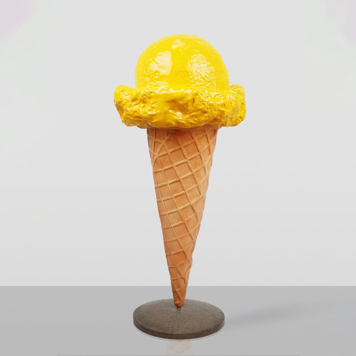 Sculpture of a yellow ice cream scoop on a waffle cone mounted on a round gray base against a plain light background.