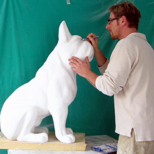 Artist working on a large white dog sculpture against a green background.