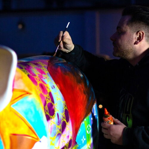 An artist painting a colorful, decorated statue.