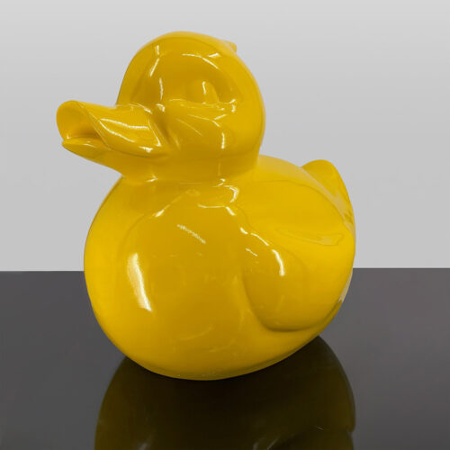 Yellow ceramic duck sculpture on a reflective surface.