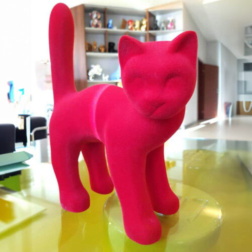 A bright pink velvet cat figurine displayed on a yellow surface in a modern room.