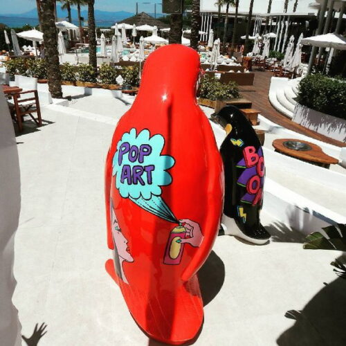 Two penguin sculptures painted in a pop art style, one red with