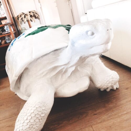 Large white tortoise statue in a living room with wooden flooring and white furniture.