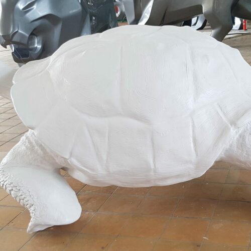 Large white tortoise sculpture in an indoor setting with tiled floor and other sculptures in the background.