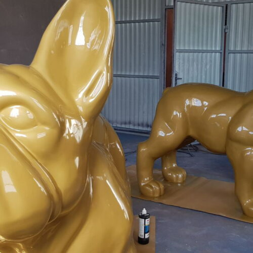 Large yellow glossy statues of French bulldogs in an industrial workshop.