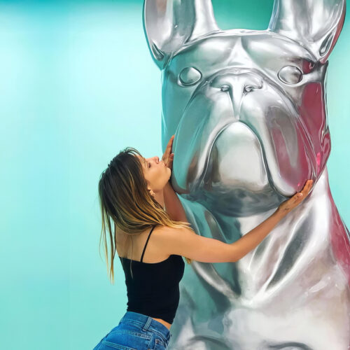 Woman embracing and kissing a large metallic sculpture of a bulldog.