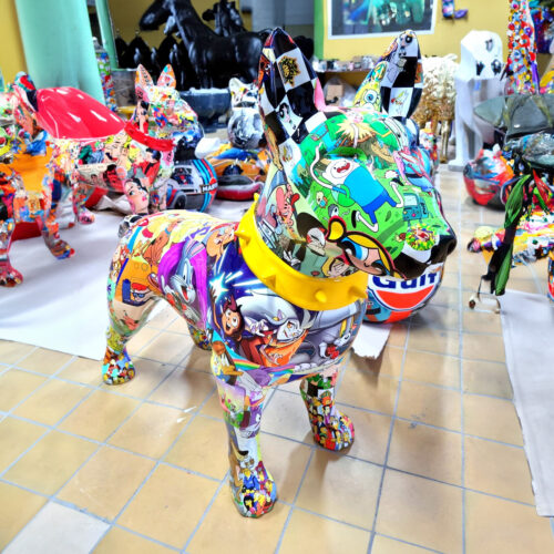 Colorful dog statue adorned with various cartoon character images, standing on a tiled floor in an art studio filled with similar decorated sculptures.