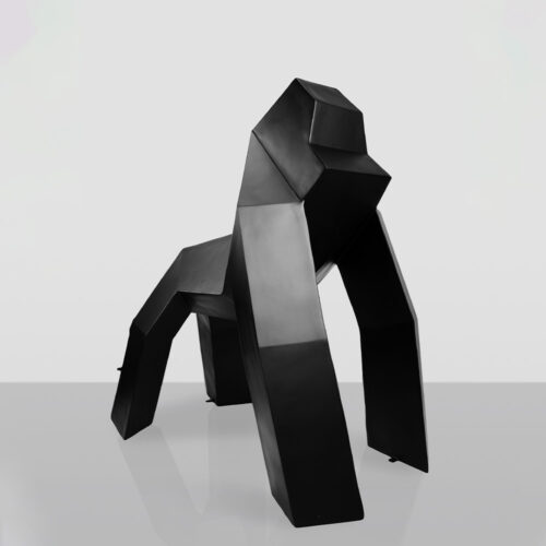 Black geometric sculpture of a gorilla in a crawling pose on a reflective gray surface with a plain light gray background