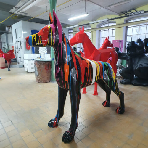 Colorful, striped statue of a dog in an art studio with other animal statues in the background.