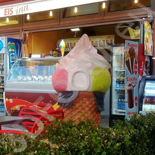 Ice cream shop with a giant ice cream cone statue at the entrance and menu boards displaying various ice cream options.