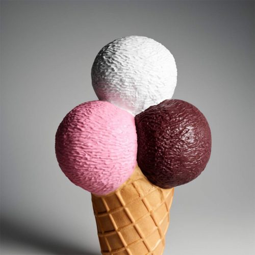 Large ice cream cone sculpture outside a striped awning ice cream shop with people sitting at outdoor tables.