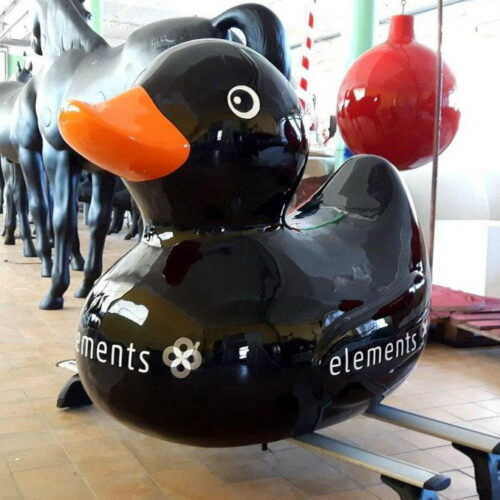A large black rubber duck sculpture with an orange beak and the word