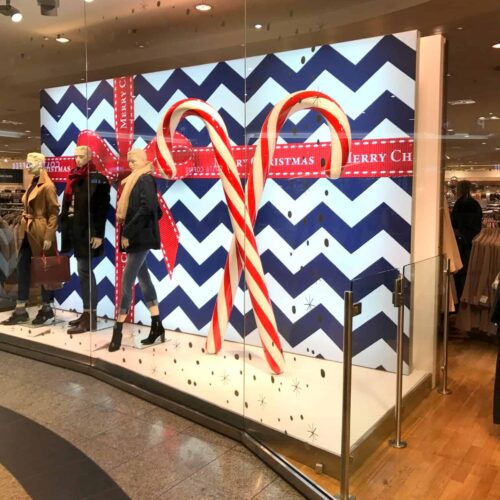 Holiday store window display with mannequins dressed in winter clothing, large candy canes, and festive