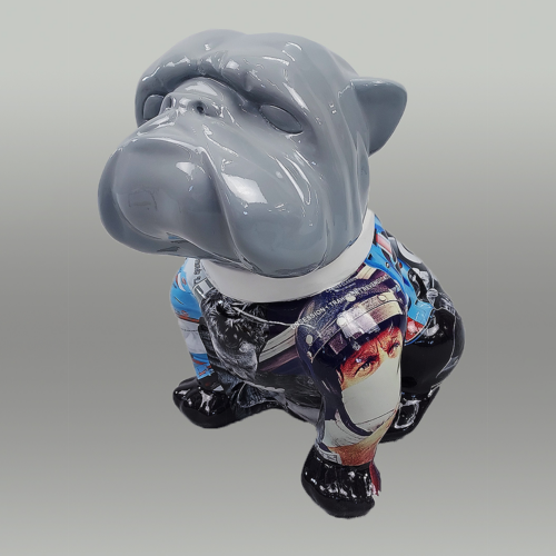 A glossy bulldog sculpture with a gray head, black legs, and a body covered in various colorful images and patterns, including a prominent face with a mask.