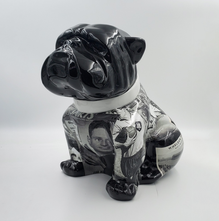 Sculpture of a sitting bulldog with a shiny black head and neck, and a body decorated with monochrome images and text clippings.