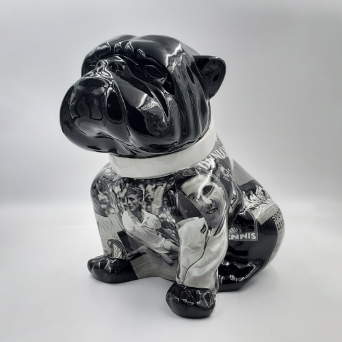 Sculpture of a sitting bulldog with a shiny black head and collar, featuring a collage of black and white tennis-themed images on its body.