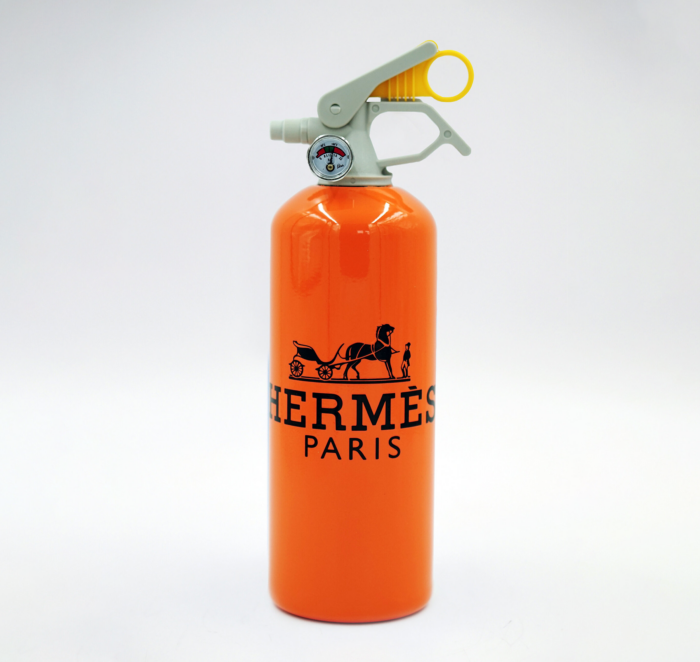 Orange fire extinguisher with Hermes Paris logo and a horse-drawn carriage graphic.