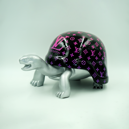 A silver turtle sculpture with a black shell featuring pink Louis Vuitton logos and patterns.