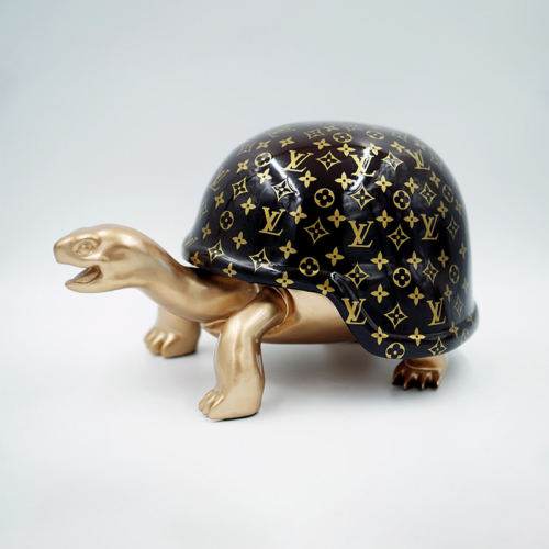 A golden figurine of a turtle with a black shell adorned with a luxury brand's monogram pattern.
