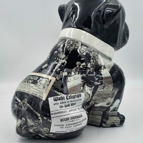 Black ceramic bulldog figurine with vintage rugby-themed newspaper clippings and black-and-white images of players.