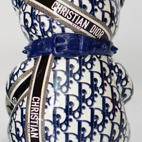 A ceramic teddy bear figurine adorned with a blue and white pattern featuring the Christian Dior logo and multiple 