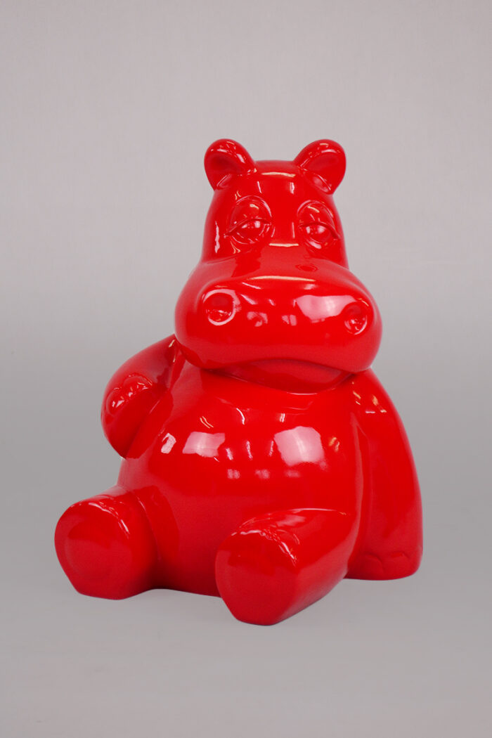 Glossy red hippopotamus-shaped sculpture sitting on a gray surface.