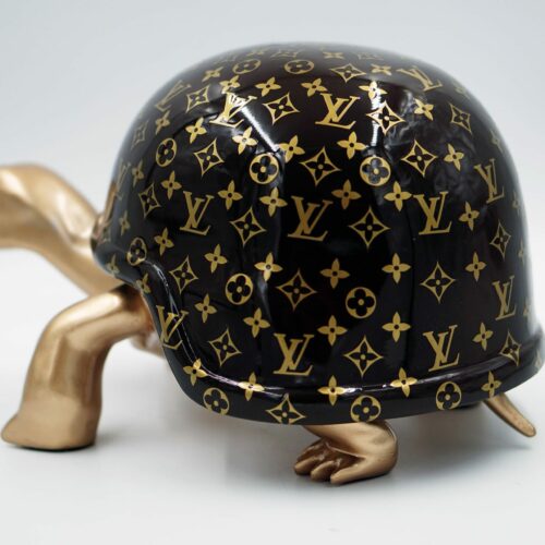 A turtle sculpture with a shiny black shell featuring a gold Louis Vuitton monogram pattern and metallic gold limbs.