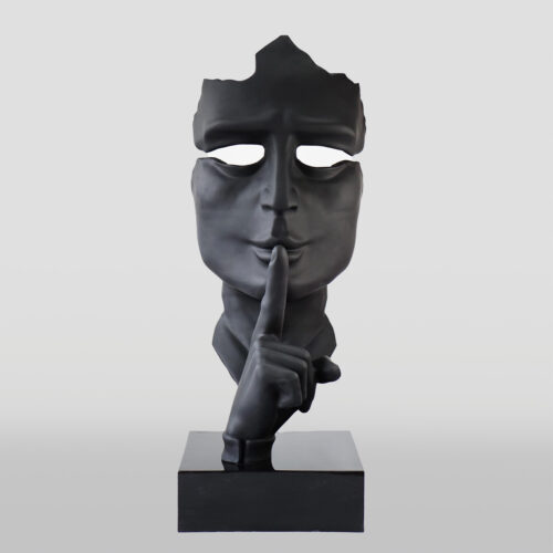 Black sculpture of a face with a broken top, hollow eyes, and a finger on the lips in a shushing gesture, mounted on a rectangular base.