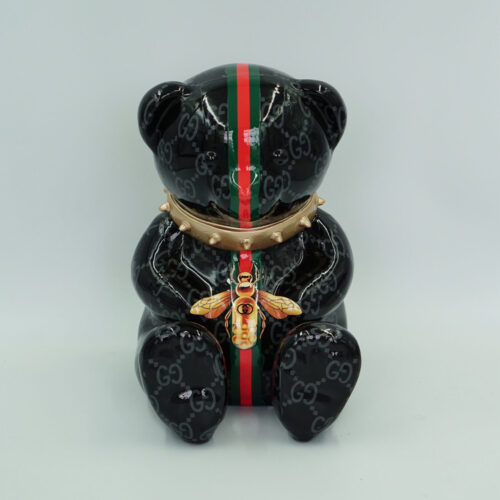 Black ceramic bear adorned with a red and green stripe, GG logo pattern, spiked gold collar, and a gold bee ornament on its chest.